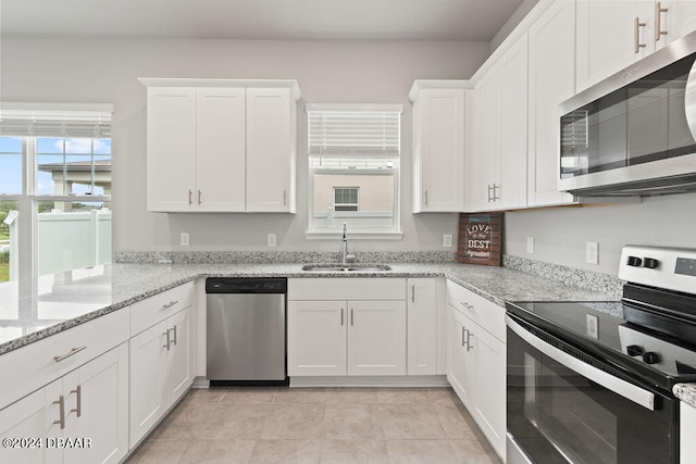 kitchen featuring white cabinets, sink, light tile patterned floors, light stone countertops, and appliances with stainless steel finishes