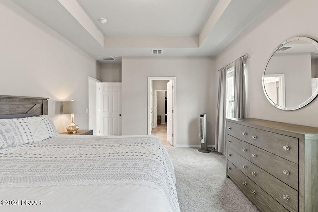 bedroom with light colored carpet and a tray ceiling