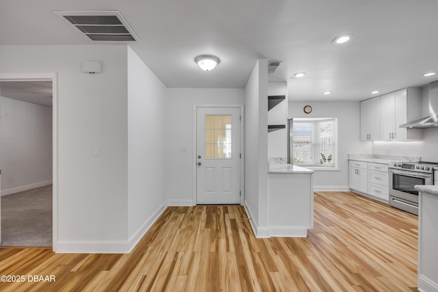 kitchen featuring stainless steel range with electric stovetop, wall chimney range hood, white cabinets, light wood-style floors, and open shelves