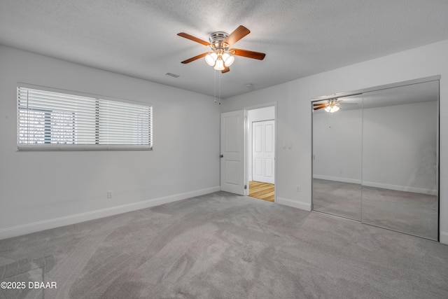 unfurnished bedroom featuring a textured ceiling, carpet floors, a closet, baseboards, and a ceiling fan