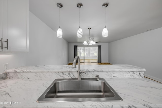 kitchen featuring a sink, light stone counters, a chandelier, and pendant lighting
