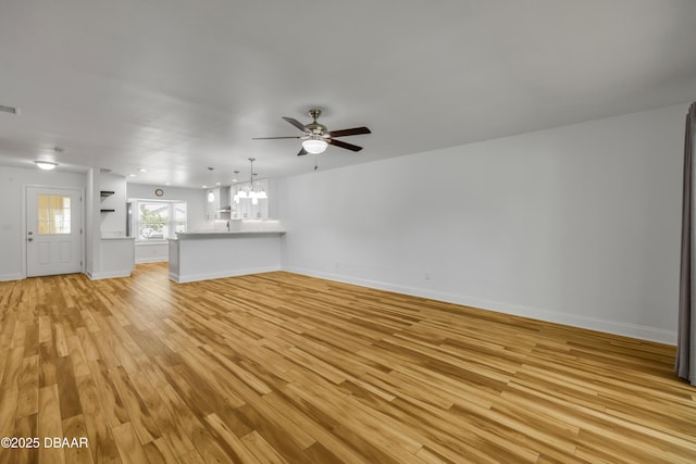 unfurnished living room with a chandelier, a ceiling fan, light wood finished floors, and baseboards