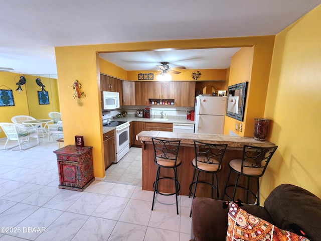 kitchen with ceiling fan, sink, kitchen peninsula, white appliances, and a breakfast bar