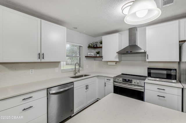 kitchen with wall chimney exhaust hood, sink, a textured ceiling, appliances with stainless steel finishes, and white cabinets