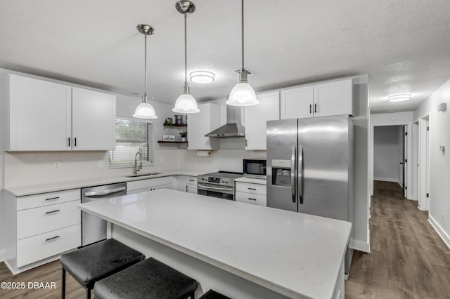 kitchen featuring white cabinets, decorative light fixtures, wall chimney exhaust hood, and appliances with stainless steel finishes