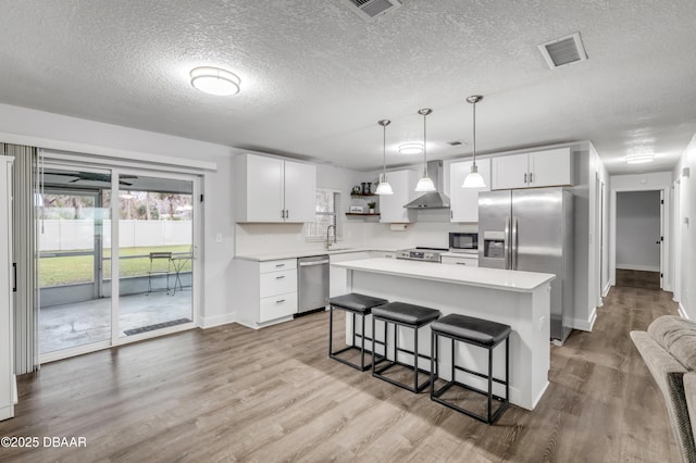 kitchen with appliances with stainless steel finishes, white cabinetry, sink, a center island, and wall chimney exhaust hood