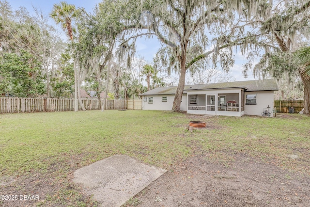 rear view of property with an outdoor fire pit, a sunroom, and a lawn