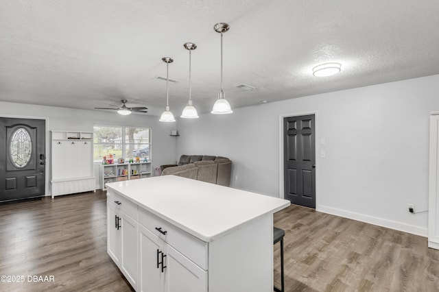 kitchen with a kitchen island, dark hardwood / wood-style floors, white cabinets, hanging light fixtures, and a textured ceiling