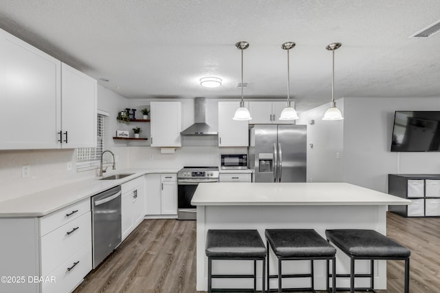 kitchen featuring appliances with stainless steel finishes, white cabinetry, sink, a center island, and wall chimney range hood