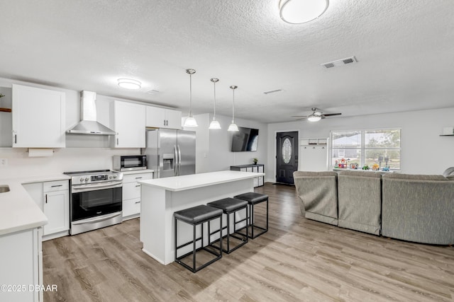 kitchen with white cabinetry, a kitchen island, wall chimney exhaust hood, and appliances with stainless steel finishes