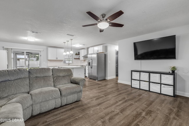 living room featuring dark wood-type flooring, a textured ceiling, and ceiling fan