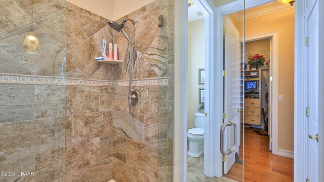 bathroom featuring toilet, hardwood / wood-style floors, tiled shower, and crown molding