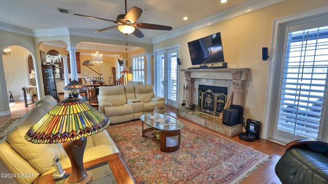 living room with crown molding, a fireplace, hardwood / wood-style floors, decorative columns, and ceiling fan with notable chandelier