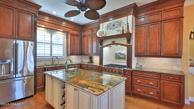 kitchen with sink, light stone counters, an island with sink, high quality appliances, and light wood-type flooring