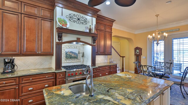 kitchen featuring light stone counters, ornamental molding, backsplash, sink, and an island with sink