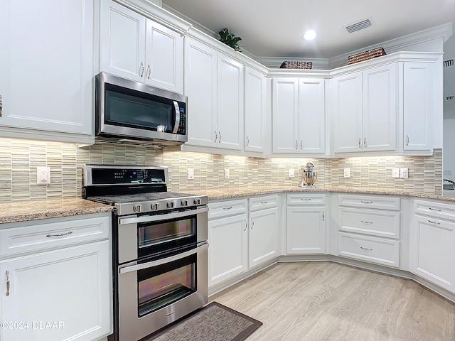 kitchen with backsplash, light stone counters, stainless steel appliances, white cabinets, and light hardwood / wood-style floors