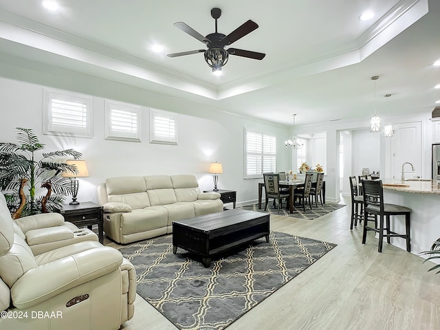 living room featuring ceiling fan with notable chandelier, light hardwood / wood-style floors, sink, and crown molding