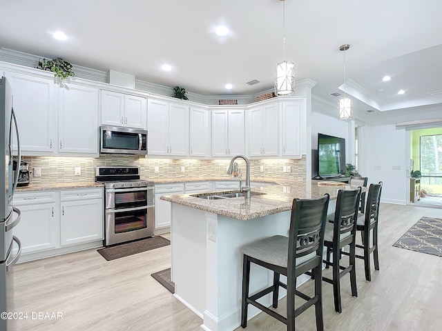 kitchen with appliances with stainless steel finishes, light wood-type flooring, ornamental molding, sink, and hanging light fixtures