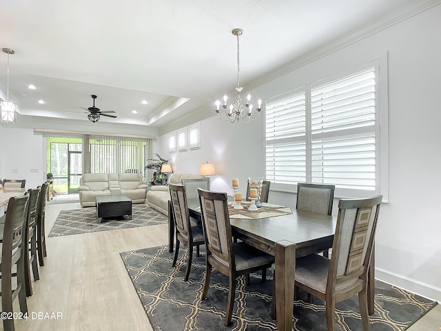 dining space with a tray ceiling, ornamental molding, ceiling fan with notable chandelier, and hardwood / wood-style flooring