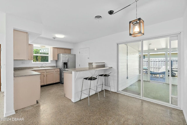 kitchen featuring kitchen peninsula, stainless steel refrigerator with ice dispenser, a kitchen breakfast bar, light brown cabinets, and hanging light fixtures