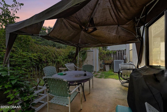 patio terrace at dusk with a storage unit, central AC, and a grill