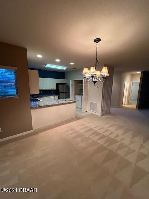 kitchen with white cabinetry, kitchen peninsula, a chandelier, decorative light fixtures, and light carpet