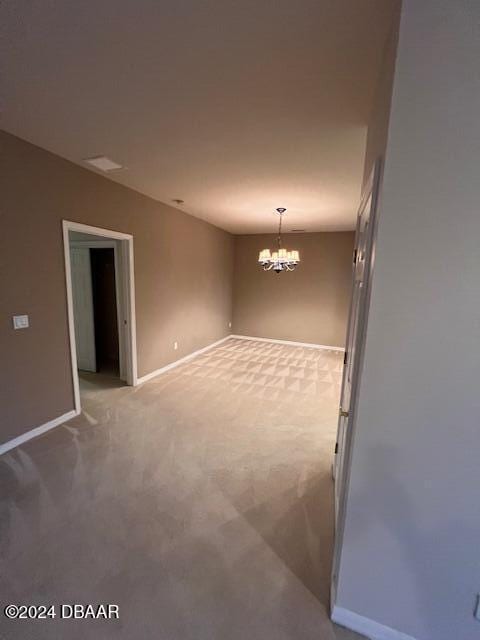 carpeted empty room featuring an inviting chandelier