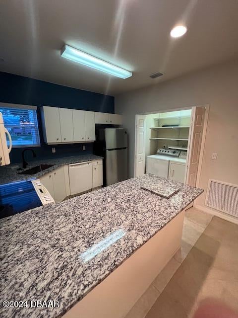 kitchen with white dishwasher, sink, stainless steel fridge, white cabinetry, and washing machine and clothes dryer