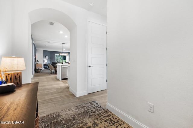 hallway with arched walkways, baseboards, visible vents, and light wood-style floors