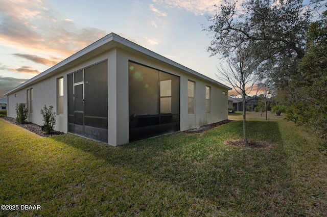 rear view of property featuring a lawn, a sunroom, and stucco siding