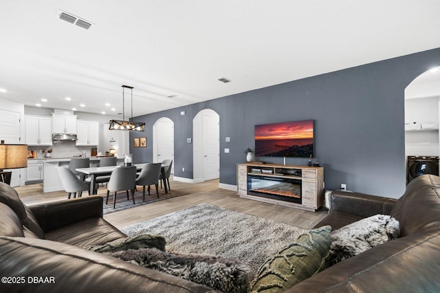 living room featuring arched walkways, washer / dryer, a glass covered fireplace, and visible vents