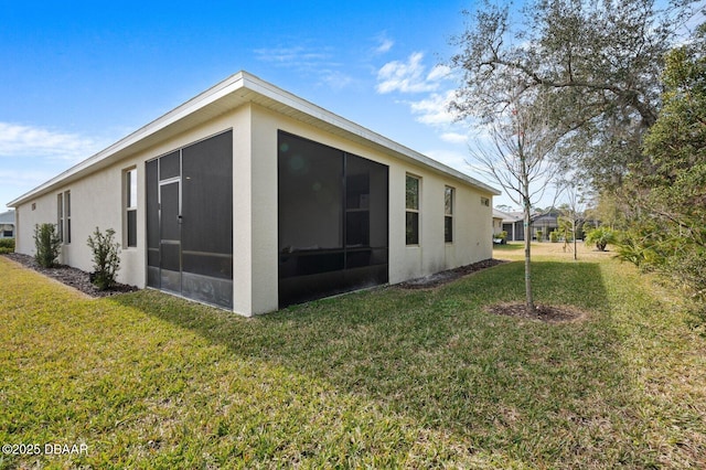 back of property with a sunroom, a lawn, and stucco siding