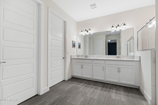 full bath featuring visible vents, a sink, a tile shower, and double vanity