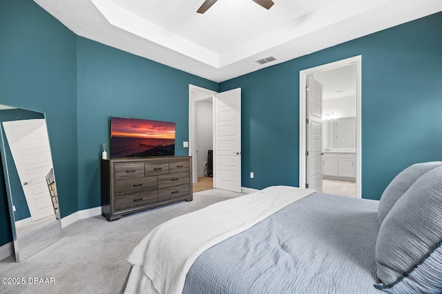 carpeted bedroom featuring a raised ceiling, visible vents, ensuite bathroom, ceiling fan, and baseboards