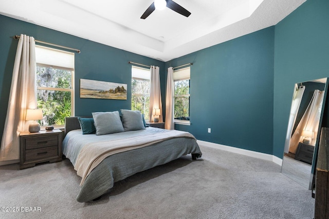 carpeted bedroom with multiple windows, baseboards, a raised ceiling, and a ceiling fan