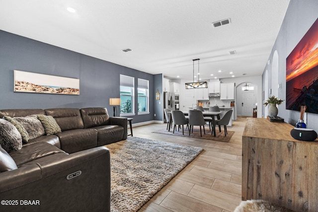 living room with visible vents, arched walkways, baseboards, wood tiled floor, and a textured ceiling