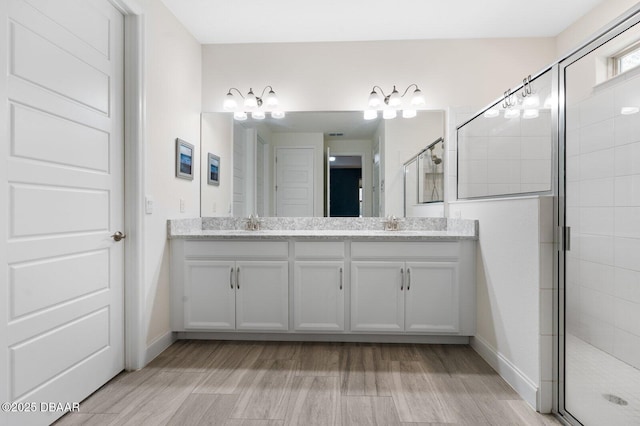 bathroom featuring wood finished floors, a sink, a shower stall, and double vanity