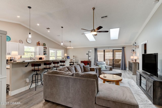 living area with ornamental molding, light wood-style floors, visible vents, and a skylight