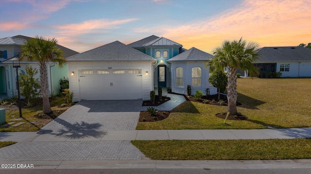 view of front of property with decorative driveway, roof with shingles, a yard, and an attached garage