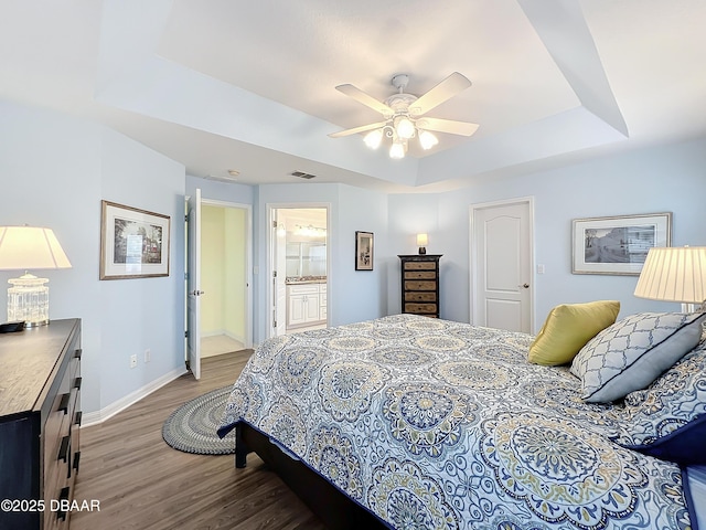 bedroom with a raised ceiling, ensuite bath, ceiling fan, and wood-type flooring