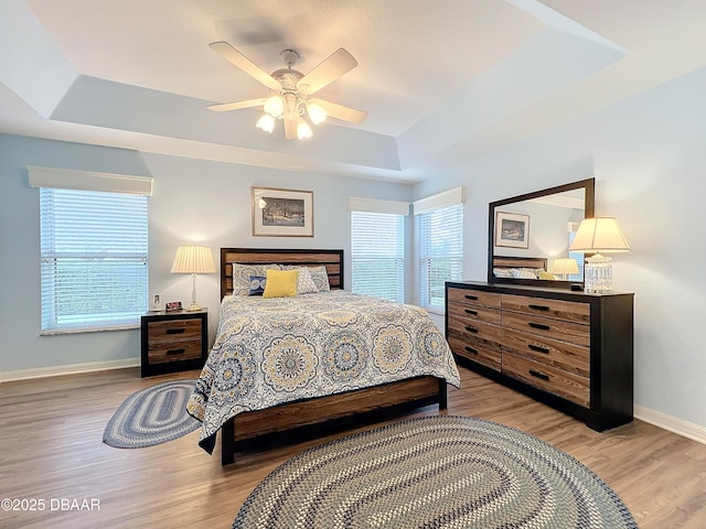 bedroom featuring ceiling fan, a raised ceiling, wood-type flooring, and multiple windows