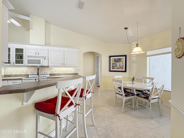 kitchen featuring white cabinets, backsplash, decorative light fixtures, stainless steel range with electric stovetop, and light tile patterned floors