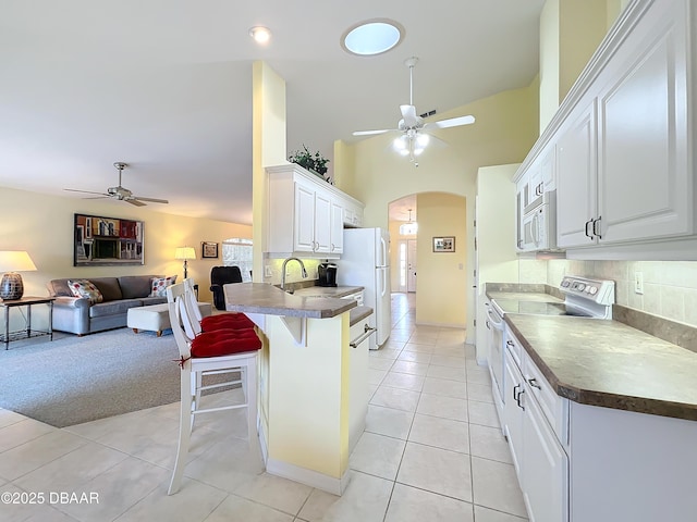 kitchen featuring white appliances, tasteful backsplash, white cabinetry, and a breakfast bar area