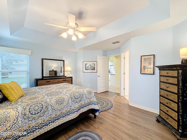 bedroom with a tray ceiling, ensuite bath, ceiling fan, and light hardwood / wood-style floors