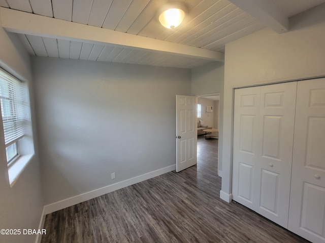 unfurnished bedroom featuring vaulted ceiling with beams, wood ceiling, baseboards, a closet, and dark wood finished floors