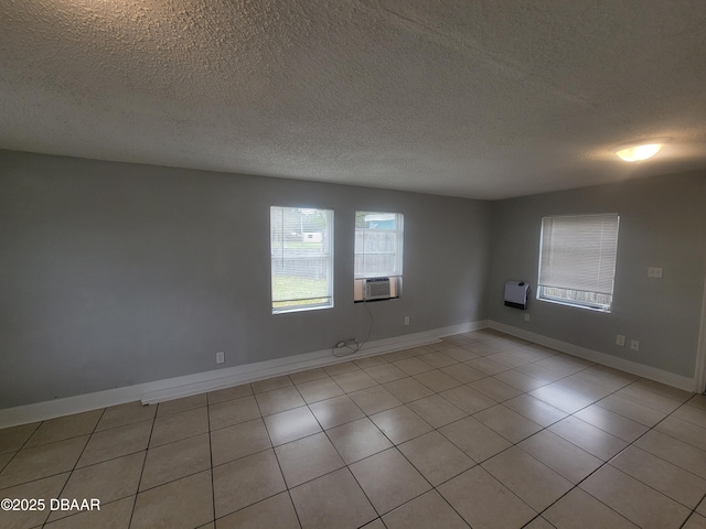 spare room with a textured ceiling, cooling unit, and baseboards