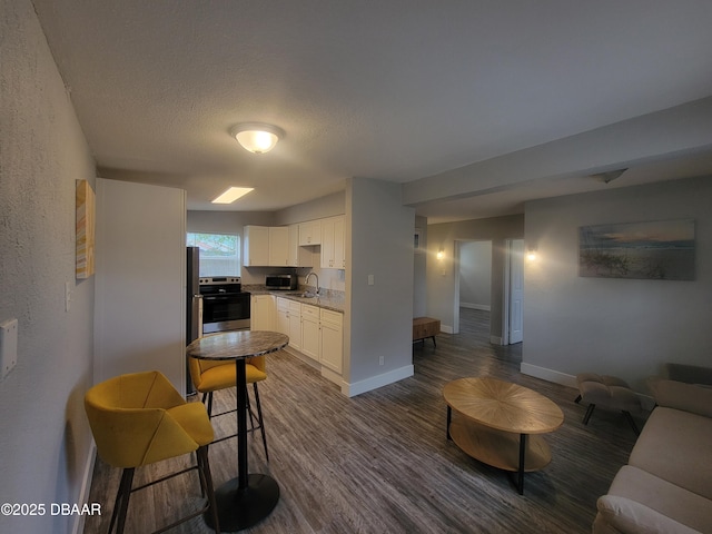 kitchen with dark wood-style flooring, stainless steel electric range, white cabinetry, a sink, and baseboards