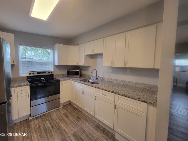 kitchen with a sink, white cabinetry, appliances with stainless steel finishes, light stone countertops, and dark wood-style floors