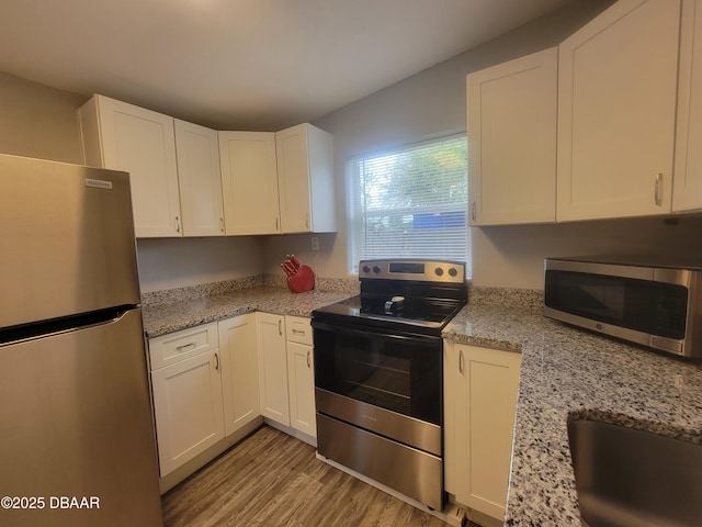 kitchen featuring appliances with stainless steel finishes, light wood-type flooring, light stone counters, and white cabinets