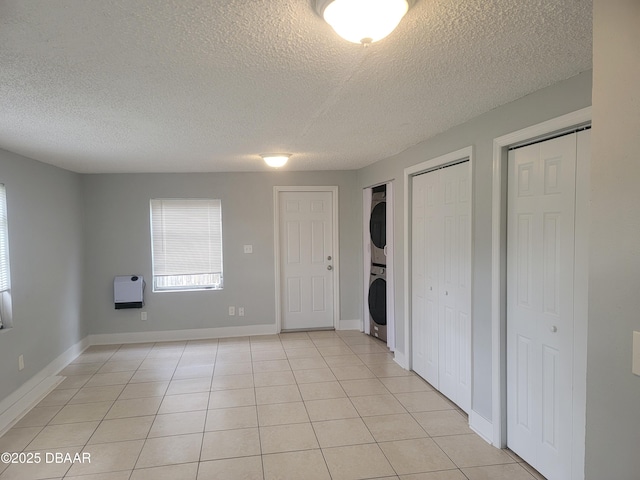 spare room with heating unit, baseboards, stacked washing maching and dryer, and light tile patterned floors